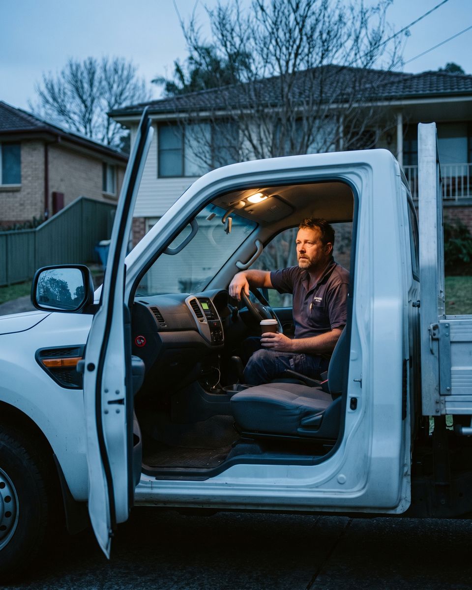 A tired tradie sitting in his ute with a coffee before sunrise